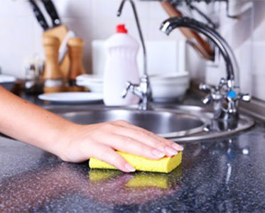 A person cleaning the kitchen counter top with a sponge.