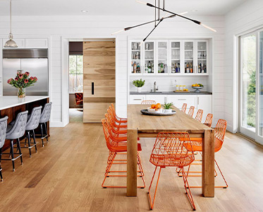 A dining room table with orange chairs and a kitchen in the background.